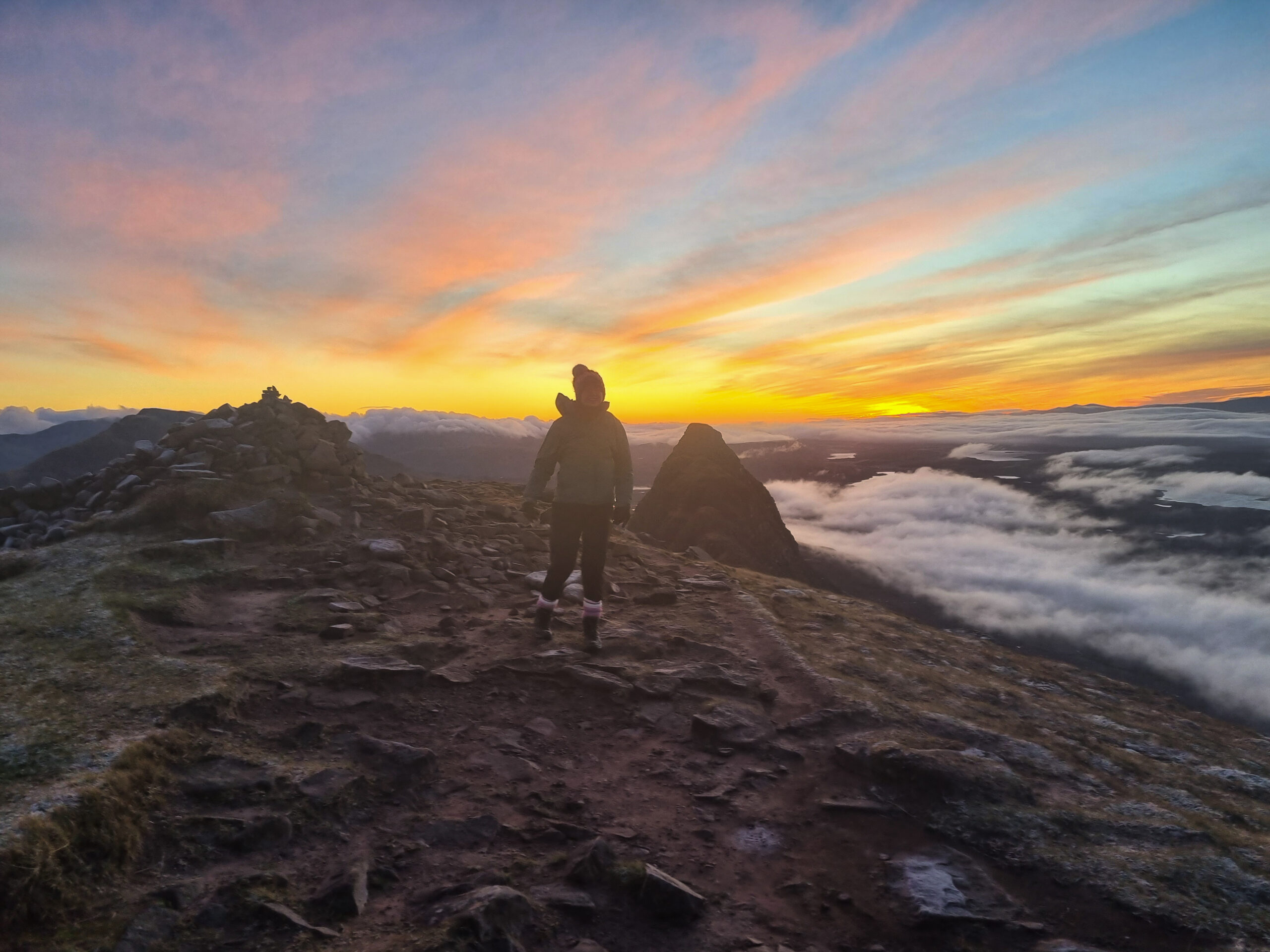 A person standing at the summit cairn of Suilven at sunrise