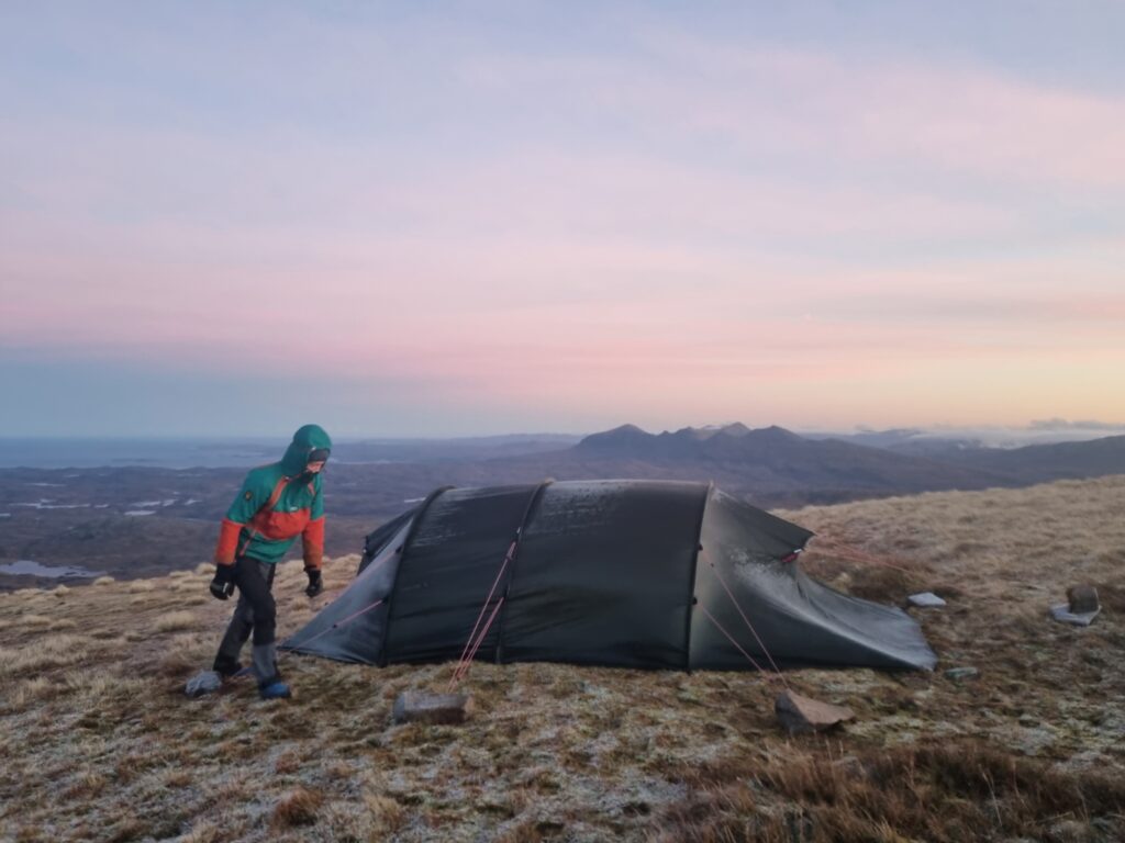 A man and tent at dawn on the summit of Suilven, Scotland with Quinag in the distance